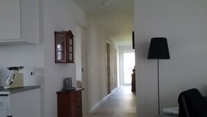 A hallway with a wooden cabinet, a scale, and a chair. - Hals Hotel Apartment (Hals)