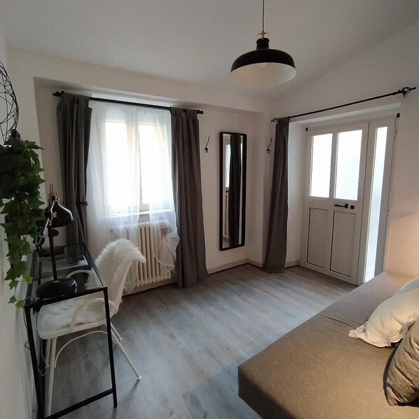 Una habitación con cama, un escritorio con silla, un radiador y una ventana con cortinas.