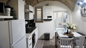 A compact kitchen with white appliances, a small trash bin, and a dining area with a table and chairs. - Romantic historic house in Atri with a view of the Gran Sasso - CIN IT067004C2D739CXUO (Atri)