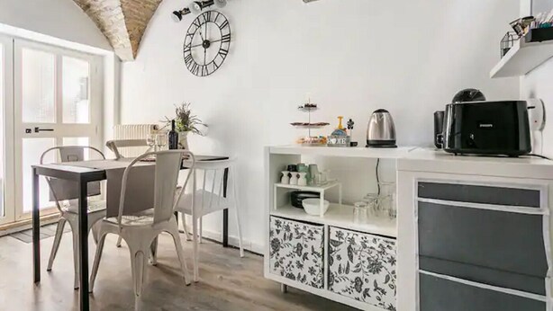 A modern kitchen with white cabinetry, a clock on the wall, and a dining area with a table and chairs. - Romantic historic house in Atri with a view of the Gran Sasso - CIN IT067004C2D739CXUO (Atri)