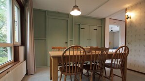 A dining area with a wooden table and chairs, a hanging light fixture, and a view through a window. - Amsterdam Farm Lodge: Ground floor apartment (Amsterdam)