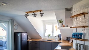 A modern kitchen with a black refrigerator, wooden countertops, and a built-in sink. There are shelves with glassware and a clock on the wall. - Sohana Lifestyle Apartments (Rust)
