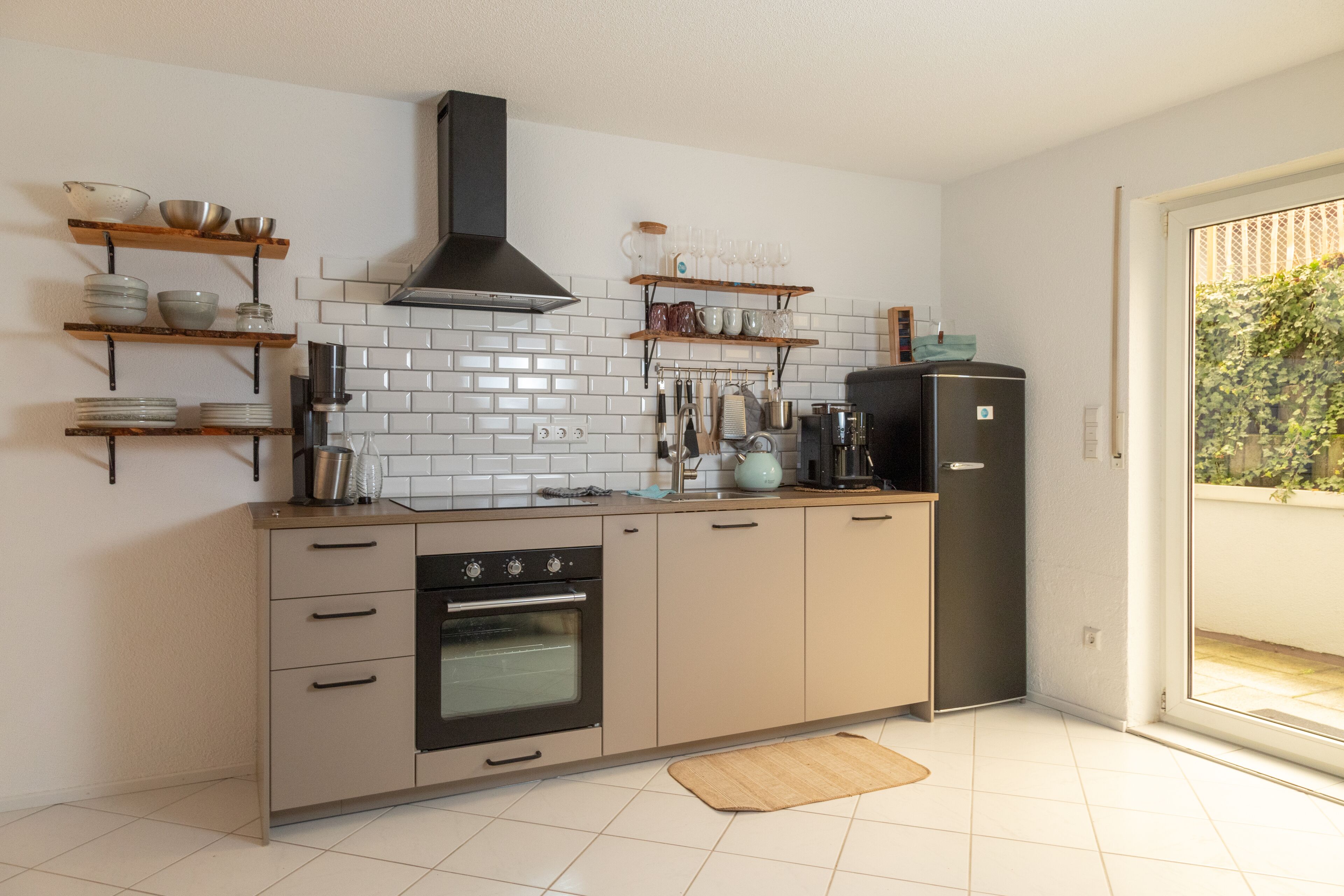 Una cucina moderna con zoccolo di piastrelle bianche, ripiani in legno e forno integrato.