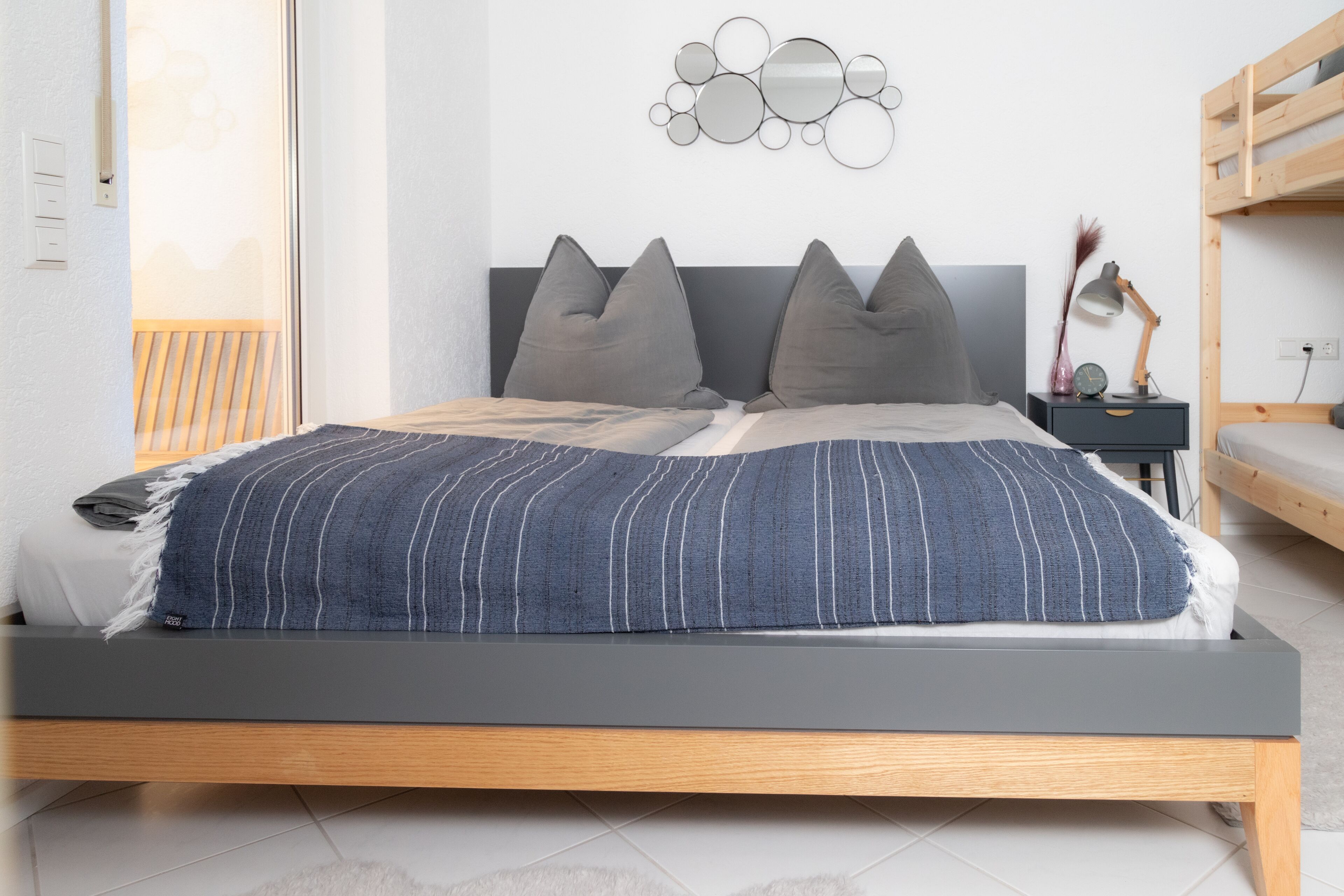 A modern bedroom with a bed, bedside tables, and a wall-mounted mirror.