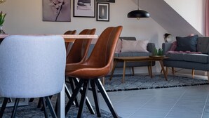 A modern dining area with a table and chairs, a sofa, and a hanging light fixture. - Sohana Lifestyle Apartments (Rust)