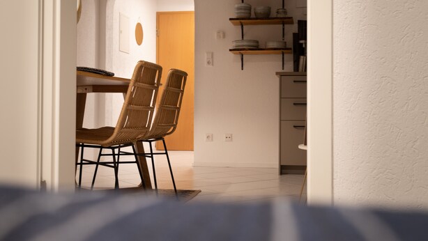 A dining area with a table and chairs, a shelf with dishes, and a door leading to another room. - Sohana Lifestyle Apartments (Rust)