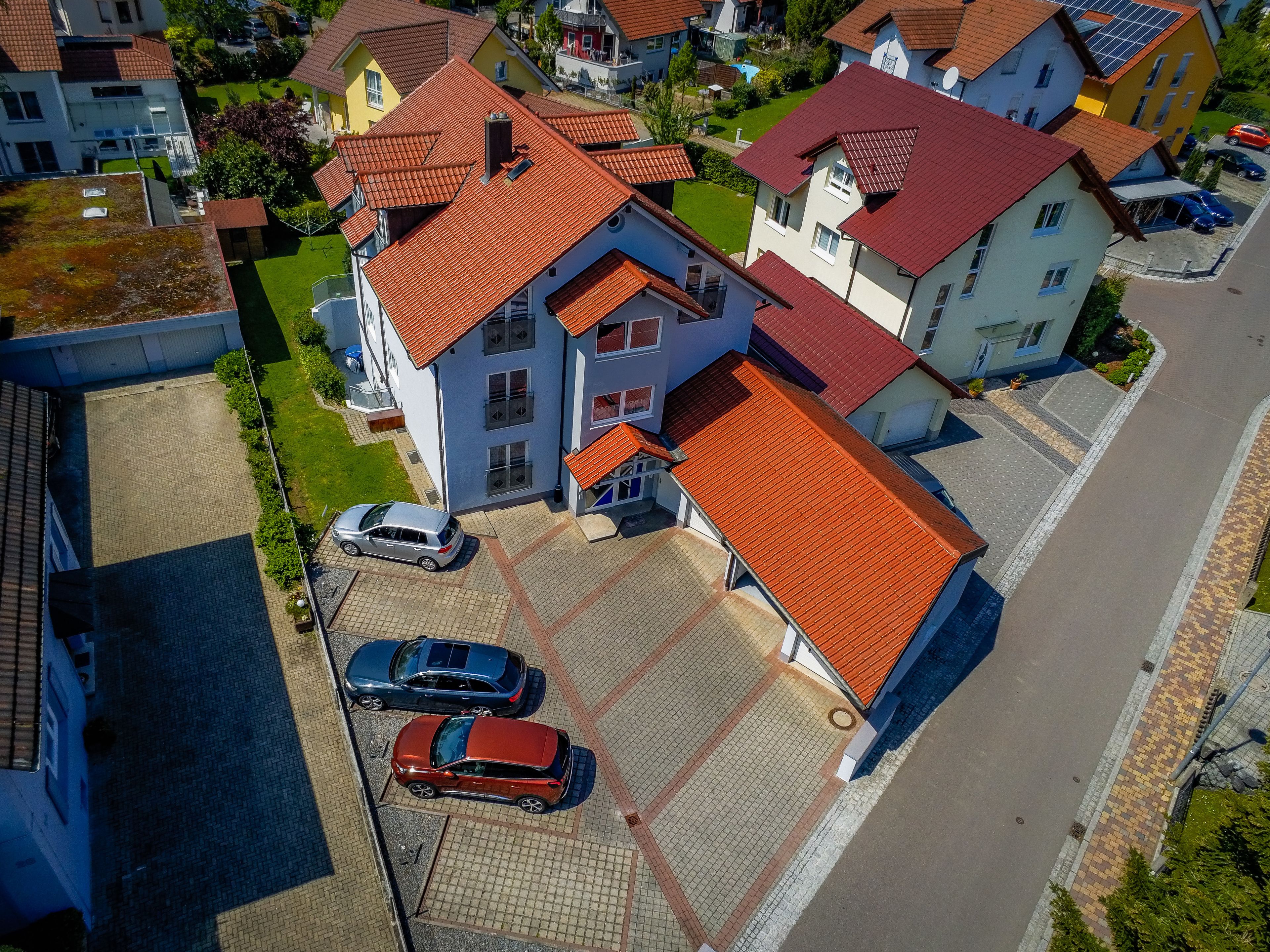 Vue aérienne d’un quartier résidentiel avec des maisons, une allée pavée et des voitures garées.