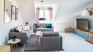 A modern living room with a grey sofa, a coffee table, and a TV on a wooden stand. - Sohana Lifestyle Apartments (Rust)