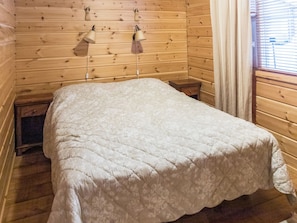 A wooden cabin room with a bed, two wall-mounted lamps, and a window with blinds. - Ylläskaira a by Interhome (Äkäslompolo)