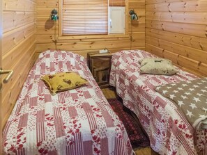 A cabin with two beds, each with a patterned bedspread, a small wooden nightstand, and a window with blinds.