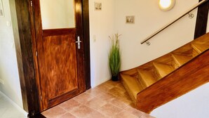 Una puerta de madera con un panel de vidrio, una pequeña planta en maceta, una escalera de madera y una lámpara en la pared.
