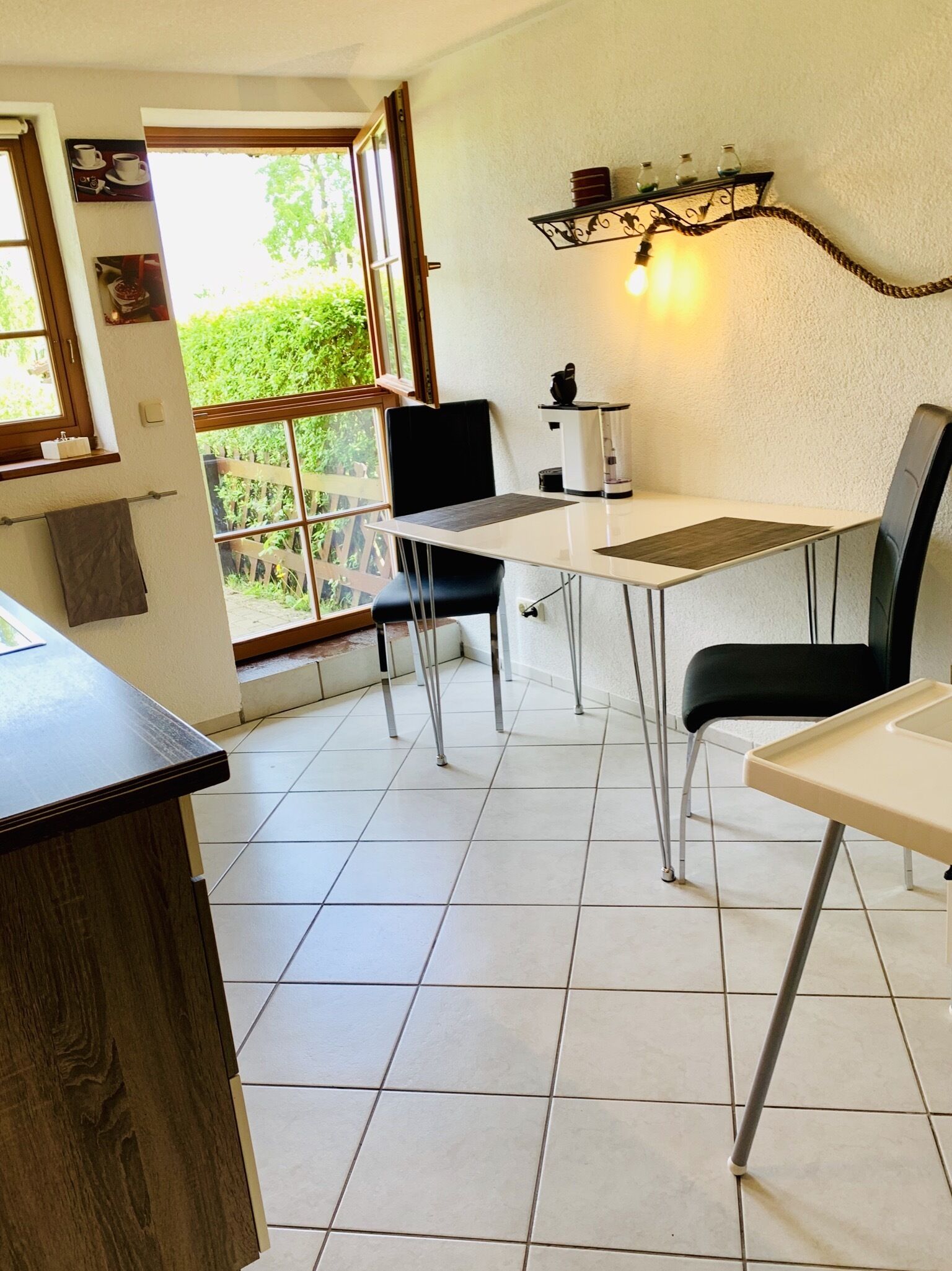 Ein Essbereich mit Tisch und Stühlen, einer Kaffeemaschine und Blick durch eine Glastür auf einen Balkon.