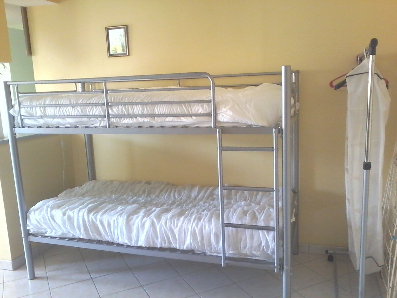 A bunk bed room with a metal frame, white bedding, and a small framed picture on the wall.