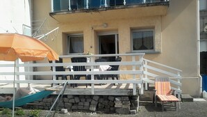 An outdoor seating area with a white railing, a table, and a chair. There is a small step leading up to the seating area, and a hammock is visible in the foreground. - rental in the heart of gerardmer (Gérardmer)