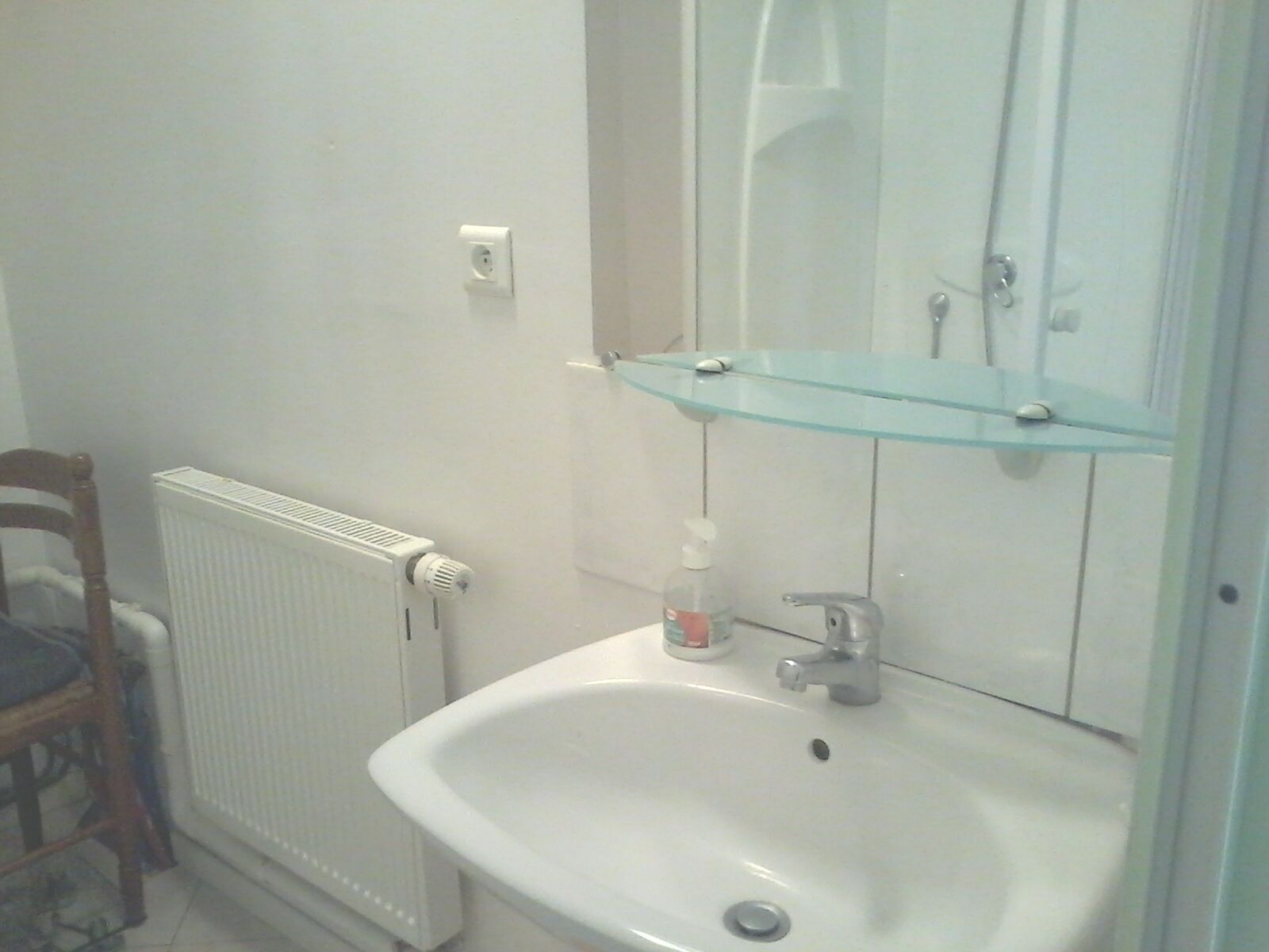 Een badkamer met een wit wastafelmeubel, een glazen plank erboven, een spiegel en een radiator.