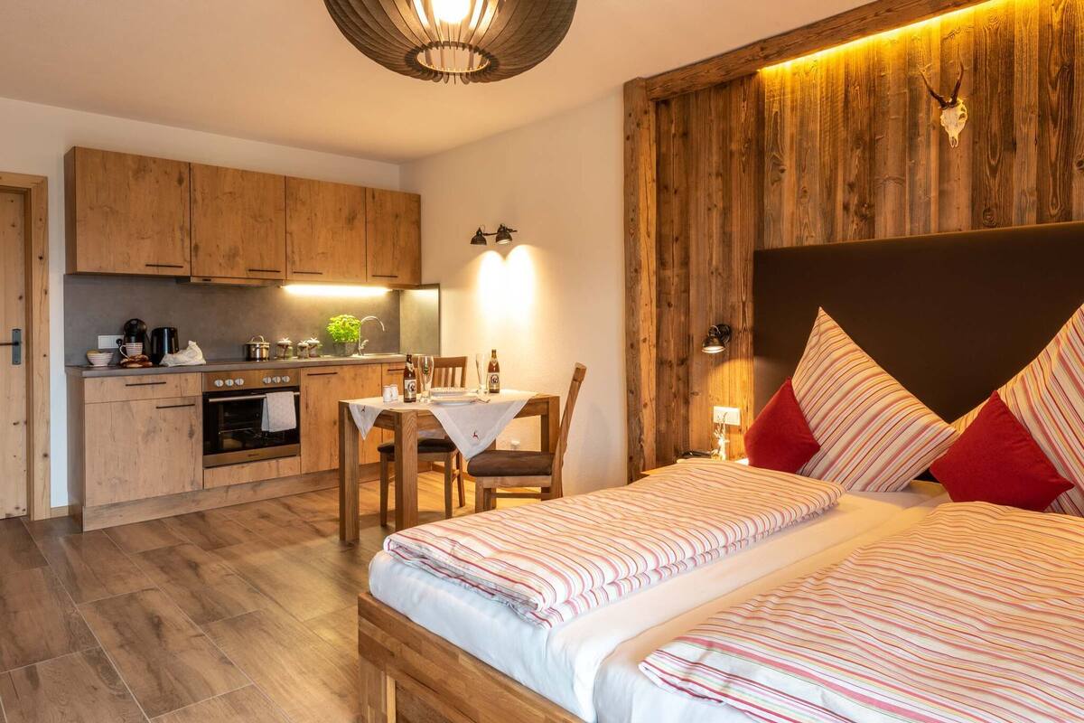 A compact room with a kitchen area, a dining table, and a bed with striped bedding.