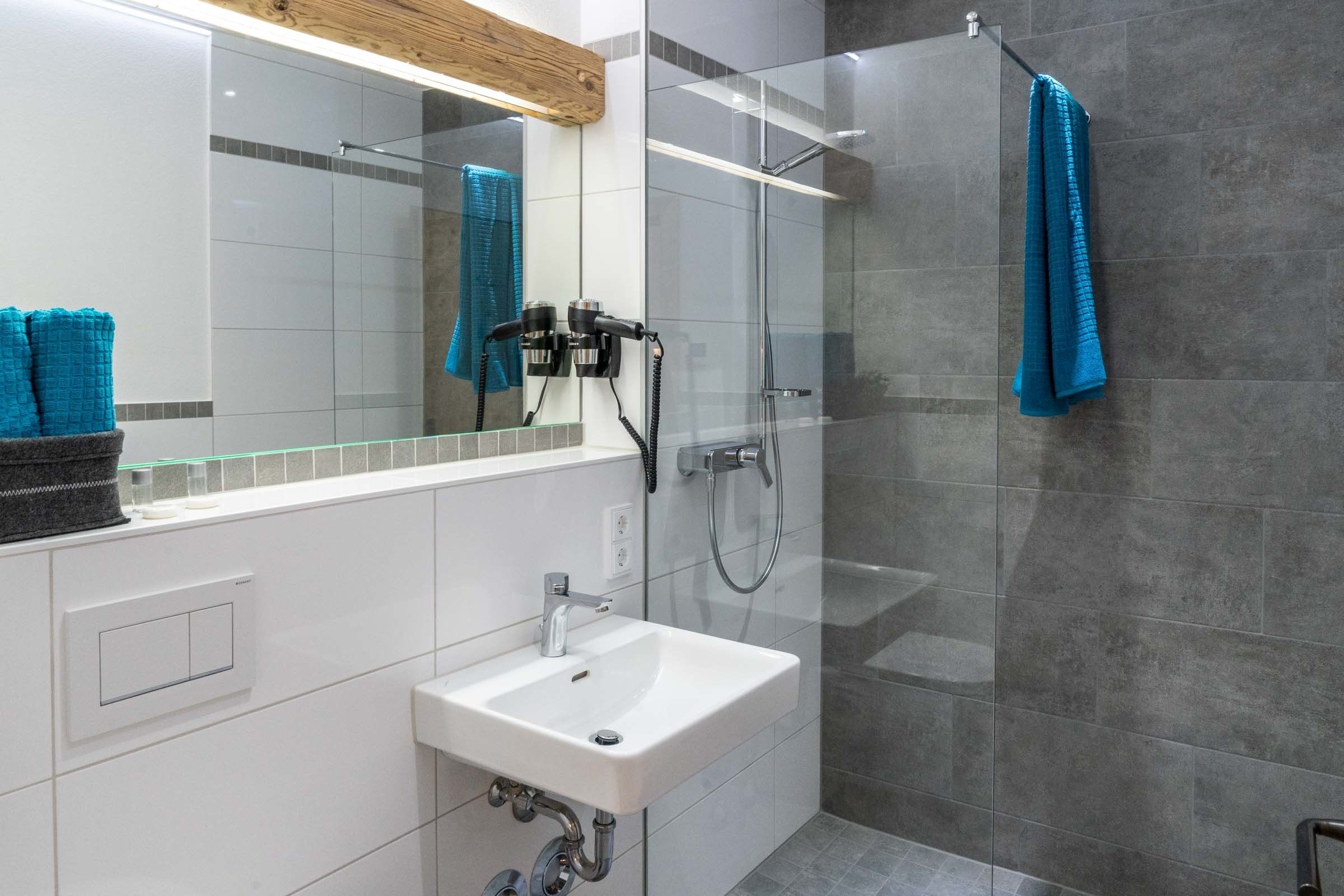 Une salle de bain moderne avec une douche à parois de verre, un lavabo blanc et un miroir au-dessus du lavabo.