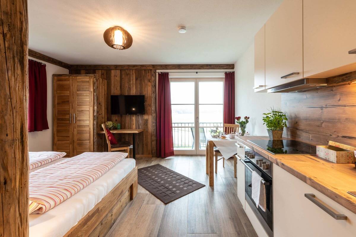 A cozy room with a bed, a desk, a TV, and a kitchen area.