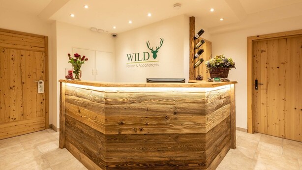 Una recepción con detalles de madera, un logotipo en la pared y una planta en maceta.