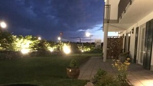 Un espacio exterior bien iluminado con una parrilla, un sendero de piedra y un edificio con grandes ventanales.