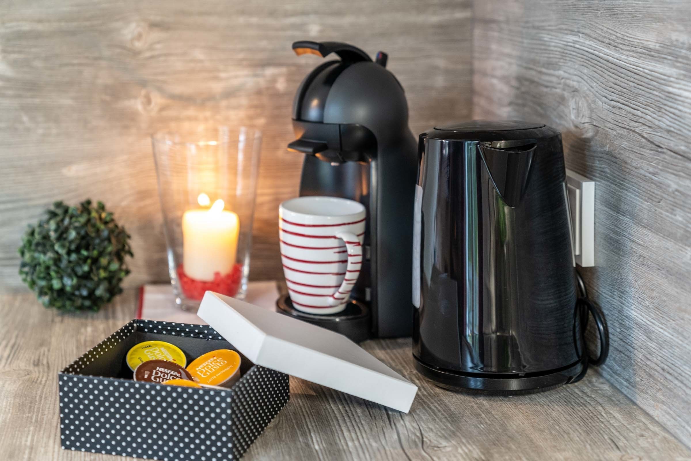 Un ambiente acogedor con cafetera, taza, vela y una caja de bombones.