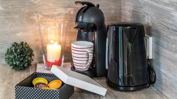 Un ambiente acogedor con cafetera, taza, vela y una caja de bombones.