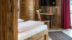 Una habitación de madera con una cama, un escritorio, una silla y un televisor en la pared.