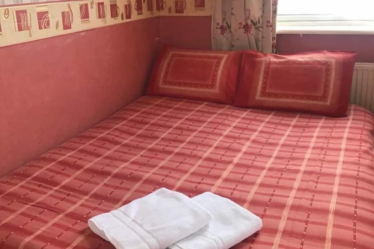 A bed with a red and white striped bedspread, two red pillows, and a folded white towel on the bed.