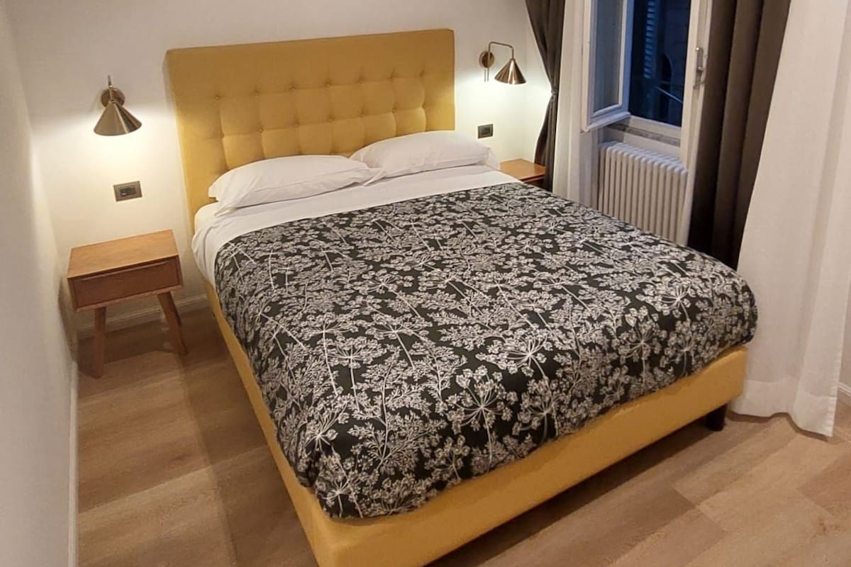 Un dormitorio con cama, un cuadro, una ventana y una mesita de noche.