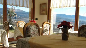 Ein Essbereich mit einem Tisch für vier Personen, Stühle mit floralem Bezug, einer Vase mit roten Blumen und Blick auf die Berge durch große Fenster.