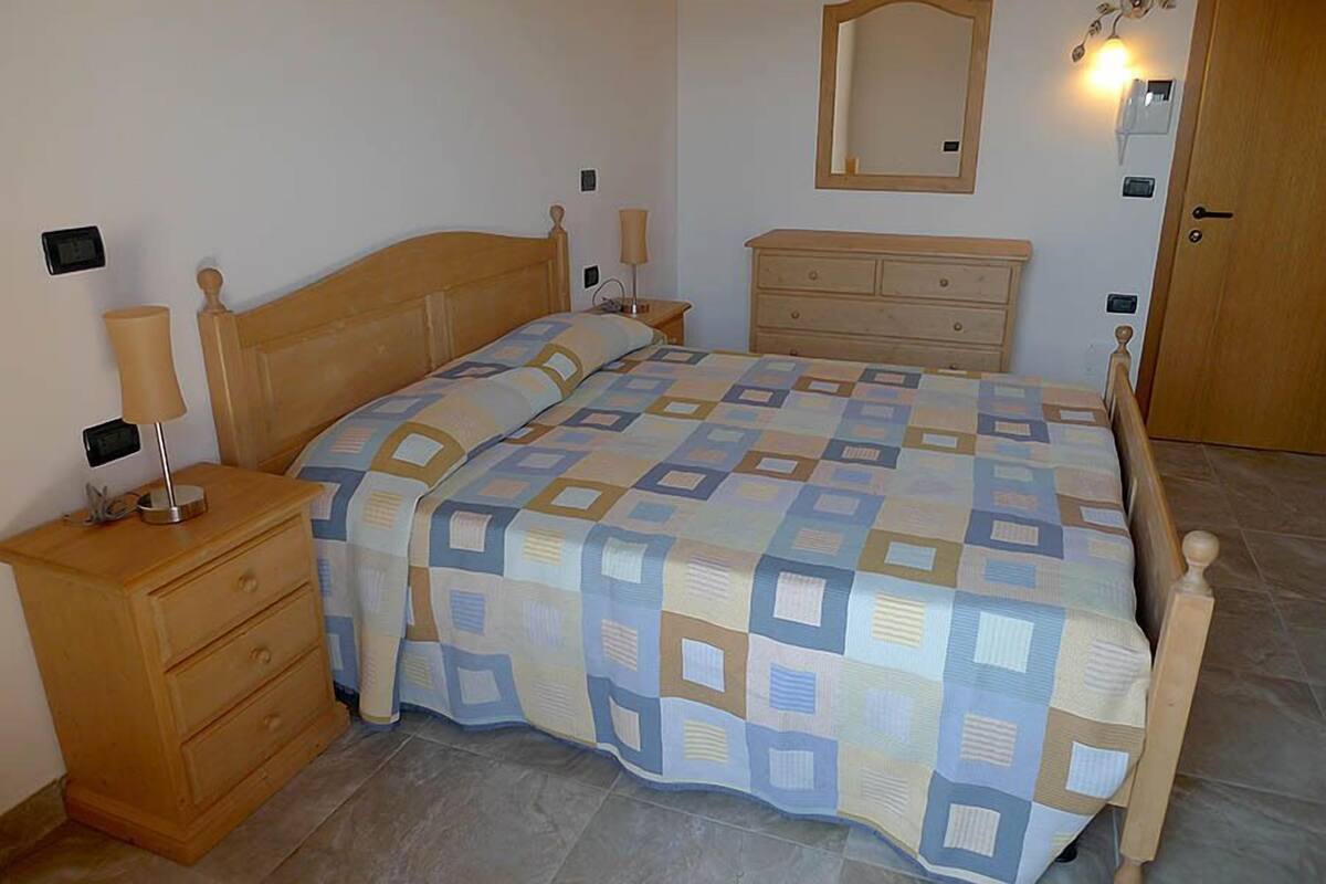 A bedroom with a wooden bed, a nightstand, a dresser, and a mirror on the wall.