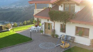Ein zweistöckiges Haus mit Terrasse, Schaukel und Blick auf einen See und Berge.