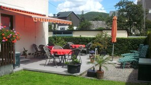 An outdoor patio with tables and chairs, a small garden area, and a view of a house in the background. - Gästehaus Andrae (Bruttig-Fankel)