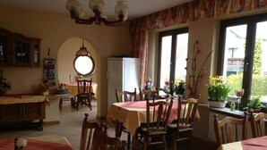 A dining area with multiple tables and chairs, a refrigerator, and a window with curtains. - Gästehaus Andrae (Bruttig-Fankel)