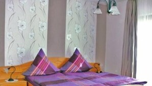 A bedroom with a wooden bed, purple bedding, a nightstand, and floral wallpaper. - Gästehaus Andrae (Bruttig-Fankel)