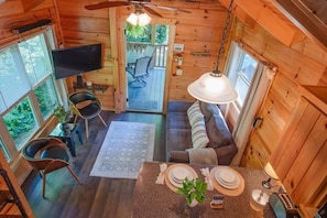 Interior acogedor de una cabaña con comedor, sofá, televisor y balcón.