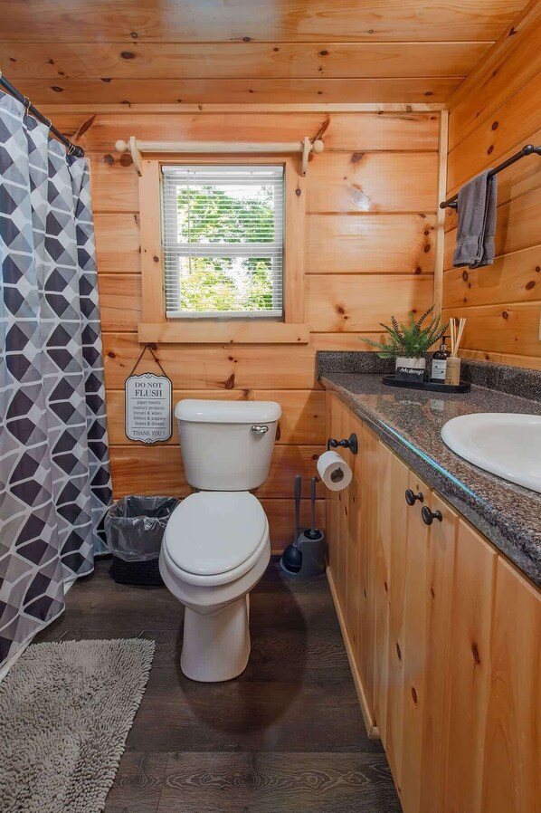 A wooden cabin bathroom with a toilet, sink, and window.