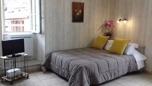 Een slaapkamer met een bed, een televisie, een tafeltje en een raam.