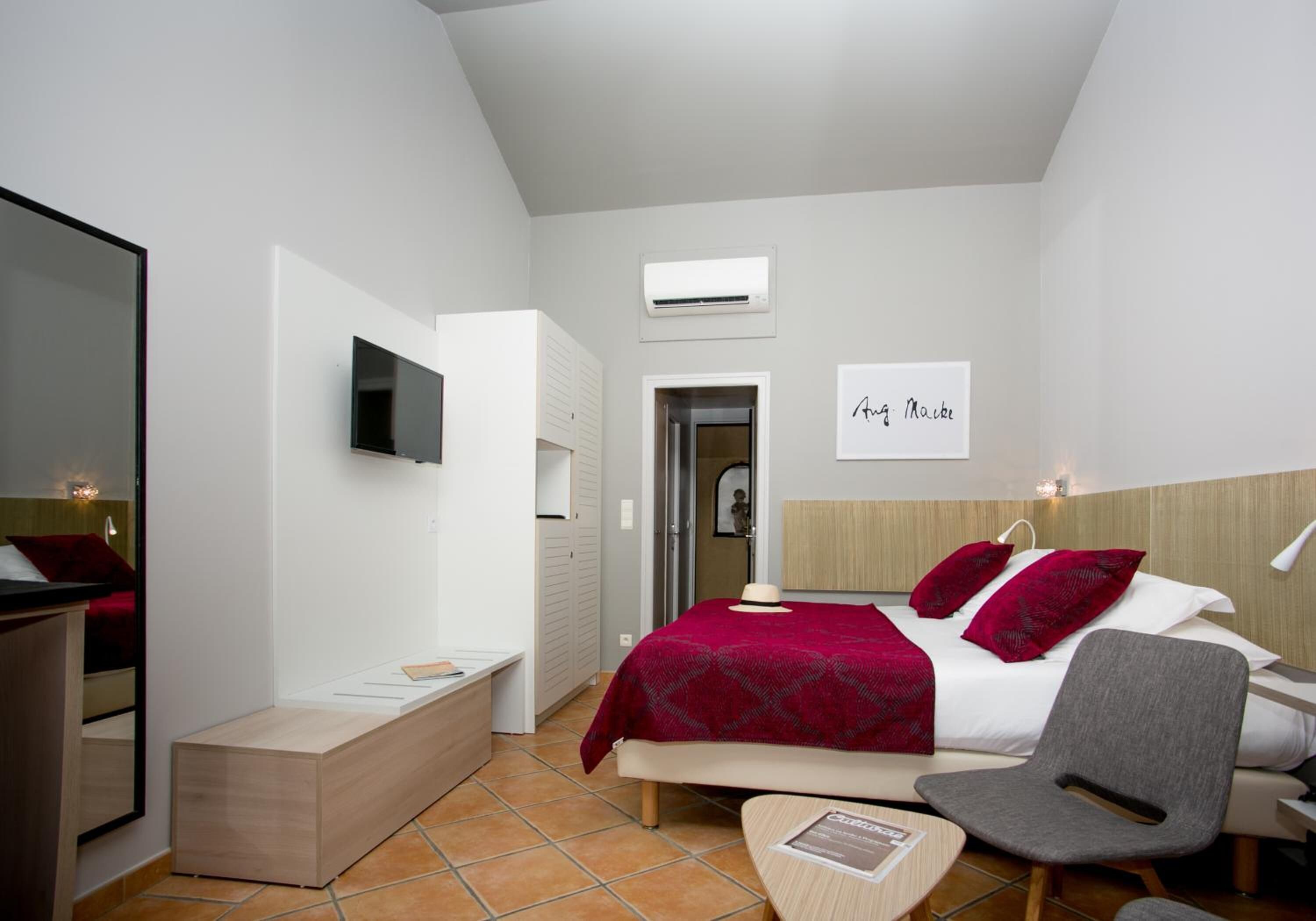 A modern hotel room with a bed, a desk, a chair, an air conditioning unit, and a television.