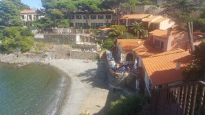 A coastal hotel with outdoor seating overlooking the beach, stone walls, and Mediterranean-style buildings. - Le Relais des trois Mas (Collioure)