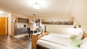A modern hotel room with a bed, desk, kitchenette, and a cityscape view. - City Hotel (Geilenkirchen)