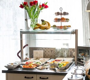 Una mesa de buffet con diversos alimentos y un jarrón de tulipanes rojos.