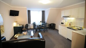 A compact hotel room with a dining area, kitchenette, and a flat-screen TV mounted on the wall. - City Hotel (Geilenkirchen)