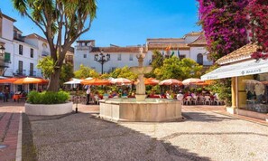 An outdoor courtyard with a central fountain, surrounded by tables and chairs under umbrellas, and a Baileys store on the right.