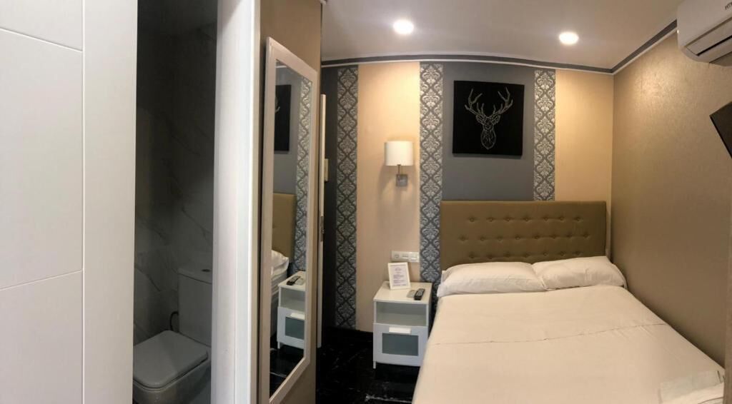 A bedroom with a bed, bedside table, nightstand, and a mirror.