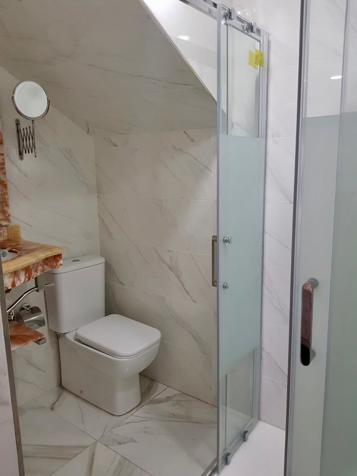 A bathroom with a glass shower enclosure, a toilet, and a marble-tiled floor.
