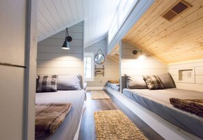 A room with two beds, a hanging light fixture, a mirror, and a window.