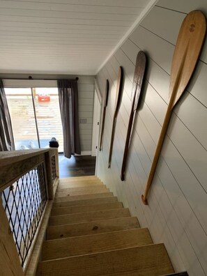 Una escalera de madera con barandilla, que conduce a una habitación de paredes blancas y vistas al exterior.