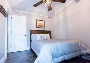 A bedroom with a bed, a ceiling fan, a door, and a framed picture on the wall.
