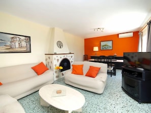 A living room with a fireplace, two sofas with orange cushions, a coffee table, and a television. - Vacation home Alma by Interhome (Calpe/Calp)